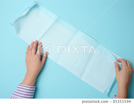 female hand holds a disposable medical diaper on a blue background. Hygiene product female hand holds a disposable medical diaper on a blue background. Hygiene product 85351594