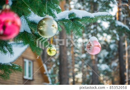 Spruce tree with Christmas toys in front of a wooden house 85352058