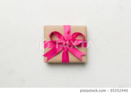 Holiday gift box wrapped in craft paper with colored bow on table background. Top view, flat lay, copy space 85352440