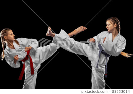 Two young girls, teens, taekwondo athletes training together isolated over dark background. Concept of sport, education, skills 85353014