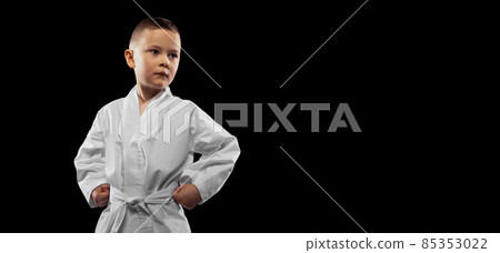 One little kid, boy, taekwondo athlete wearing white dobok isolated over dark background. Concept of sport, education, skills One little kid, boy, taekwondo athlete wearing white dobok isolated over dark background. Concept of sport, education, skills 85353022