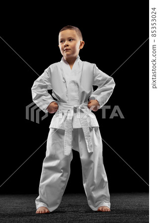 One little kid, boy, taekwondo athlete wearing white dobok isolated over dark background. Concept of sport, education, skills One little kid, boy, taekwondo athlete wearing white dobok isolated over dark background. Concept of sport, education, skills 85353024