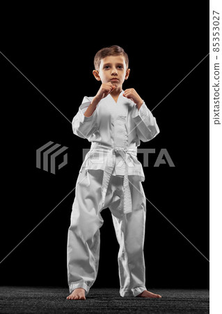 One little kid, boy, taekwondo athlete wearing white dobok isolated over dark background. Concept of sport, education, skills One little kid, boy, taekwondo athlete wearing white dobok isolated over dark background. Concept of sport, education, skills 85353027