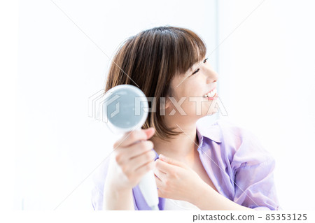 婦女用吹風機烘乾她的頭髮。 85353125