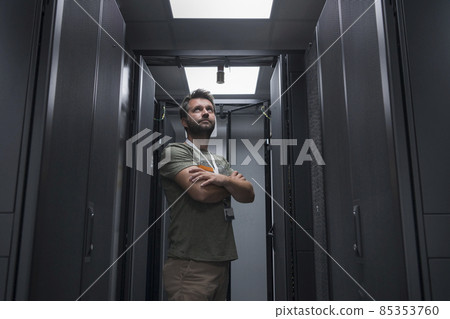 Portrait of male technician or network administrator standing brave as a hero with arms crossed in data center server room. Portrait of male technician or network administrator standing brave as a hero with arms crossed in data center server room. 85353760