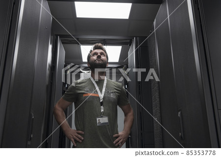 Portrait of male technician or network administrator standing brave as a hero with arms crossed in data center server room. 85353778