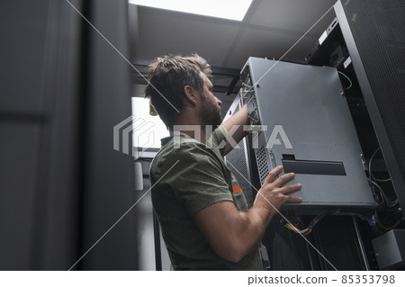 IT engineer working In the server room or data center The technician puts in a rack a new server of corporate business mainframe supercomputer or cryptocurrency mining farm. IT engineer working In the server room or data center The technician puts in a rack a new server of corporate business mainframe supercomputer or cryptocurrency mining farm. 85353798