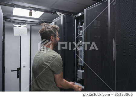 IT engineer working In the server room or data center The technician puts in a rack a new server of corporate business mainframe supercomputer or cryptocurrency mining farm. IT engineer working In the server room or data center The technician puts in a rack a new server of corporate business mainframe supercomputer or cryptocurrency mining farm. 85353806
