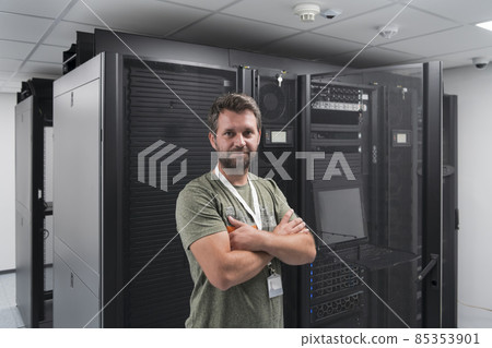 Portrait of male technician or network administrator standing brave as a hero with arms crossed in data center server room. Portrait of male technician or network administrator standing brave as a hero with arms crossed in data center server room. 85353901