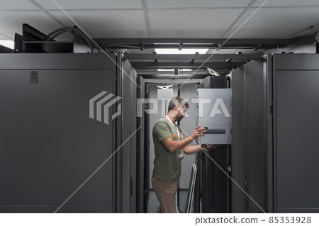 IT engineer working In the server room or data center The technician puts in a rack a new server of corporate business mainframe supercomputer or cryptocurrency mining farm. IT engineer working In the server room or data center The technician puts in a rack a new server of corporate business mainframe supercomputer or cryptocurrency mining farm. 85353928