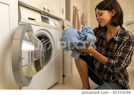 Girl puts clothes in washing mashine. 85354298