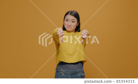 Displeased woman showing thumbs down on camera in studio 85354315