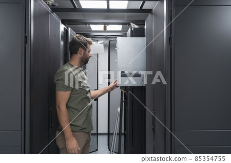 IT engineer working In the server room or data center The technician puts in a rack a new server of corporate business mainframe supercomputer or cryptocurrency mining farm. IT engineer working In the server room or data center The technician puts in a rack a new server of corporate business mainframe supercomputer or cryptocurrency mining farm. 85354755