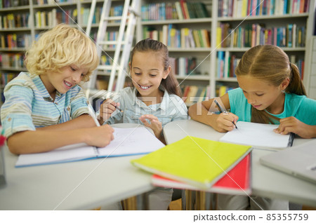 Boy and two girls writing and painting in library Boy and two girls writing and painting in library 85355759
