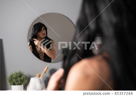 Homosexual preening in front of the mirror. A transgender man combing a wig. Homosexual preening in front of the mirror. A transgender man combing a wig. 85357284