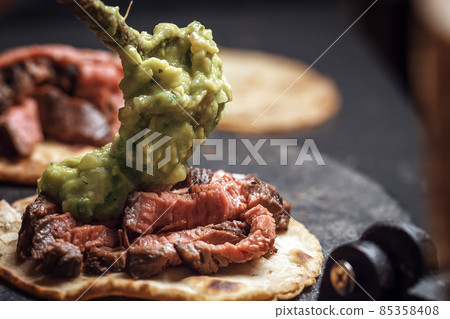 Process of cooking tacos with grilled flank beef steak with handmade guacomole 85358408