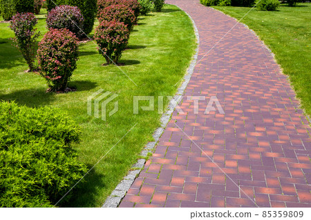curved stone tile pavement curved path in park landscaped with green grass and foliage bushes, garden landscape design of backyard on a sunny summer day, nobody. 85359809