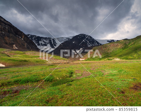 Green summer Alpine plateau on a sunny day under a dramatic dark sky. Green summer Alpine plateau on a sunny day under a dramatic dark sky. 85359815