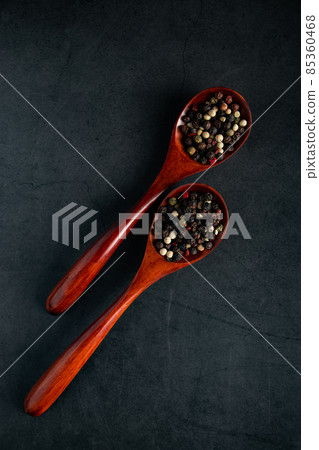 Wooden spoon with mix of pepper on a black background. Dried aromatic spice. 85360468