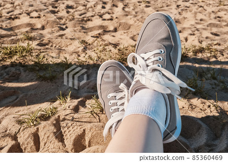 Legs in gray sneakers on the beach sand. Summer vacation concept by the sea. Lifestyle travel. Pov view. Copy space. 85360469