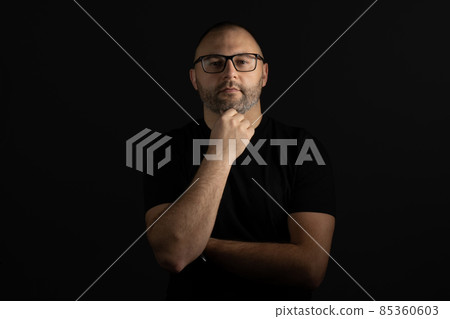 A man with glasses poses with his hand under his chin looking at the camera 85360603