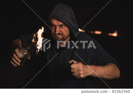 The man in the hood is holding a burning bottle. Molotov cocktail. The man in the hood is holding a burning bottle. Molotov cocktail. 85362560