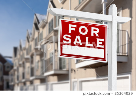 For Sale Real Estate Sign In Front of a Row of Apartment Condominiums Balconies and Garage Doors. 85364029