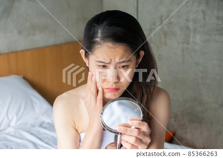 Portrait of Asian woman worry about her face when she saw the problem of acne and scar by the mini mirror. Conceptual shot of Acne & Problem Skin on female face. Portrait of Asian woman worry about her face when she saw the problem of acne and scar by the mini mirror. Conceptual shot of Acne & Problem Skin on female face. 85366263