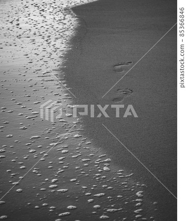 foam bubbles of the sea waves and the footprints on the beach black and white photograph. foam bubbles of the sea waves and the footprints on the beach black and white photograph. 85366846