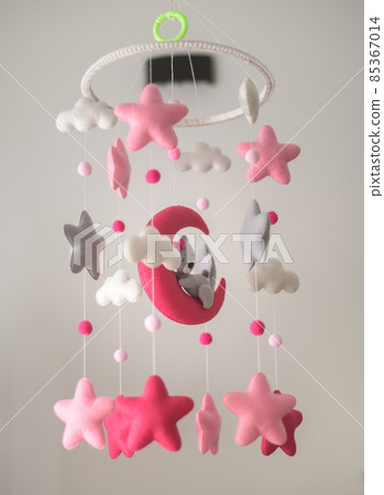 Baby crib hangings, Felt cot mobile with soft plushie stars clouds and moon with sleeping teddy, Cot isolated against a neutral color background. Beautiful music toy over the crib in the baby room. 85367014