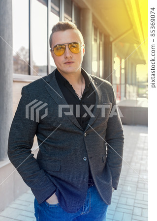 Stylish young attractive guy of European appearance businessman portrait in jacket, shirt and jeans, in sunglasses on the street outdoor 85369074