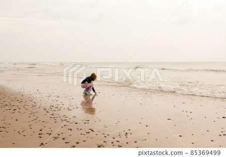 North Sea beach in Denmark at cloudy day. Small girl collecting stones. 85369499