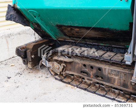 Fragment of a rusted asphalt paver track standing on a concrete surface outdoors Fragment of a rusted asphalt paver track standing on a concrete surface outdoors 85369731