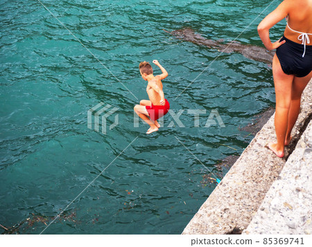 Boy in red swimming trunks jumping into the sea with his legs bent 85369741