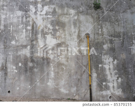 A gray concrete wall with dark and light spots and a yellow metal pipe connected to it 85370155