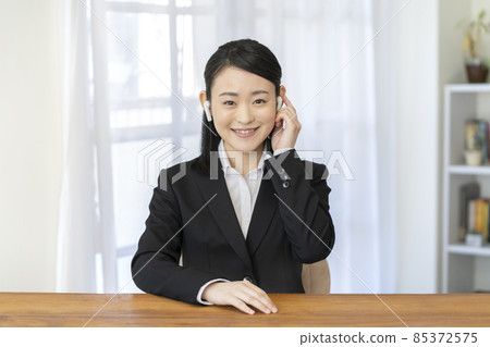 A young woman in a smiling suit wearing wireless earphones and talking looking at the camera A young woman in a smiling suit wearing wireless earphones and talking looking at the camera 85372575