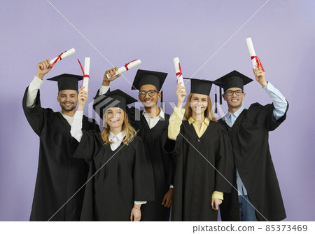 Congrats, grad. Happy proud smiling joyful diverse international university students in graduate caps and gowns raise up paper diplomas with red ribbon standing on color background at graduation event Congrats, grad. Happy proud smiling joyful diverse international university students in graduate caps and gowns raise up paper diplomas with red ribbon standing on color background at graduation event 85373469