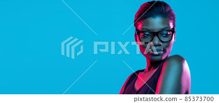 Flyer with young beautiful dark skinned woman posing isolated on blue studio background in neon light. Flyer with young beautiful dark skinned woman posing isolated on blue studio background in neon light. 85373700