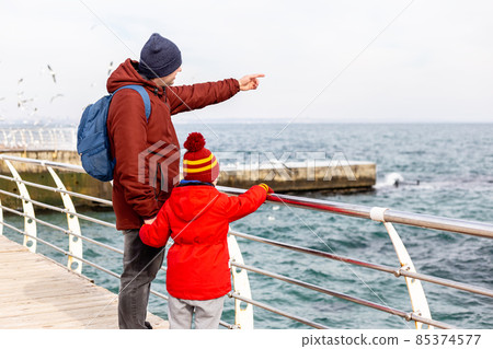 Father and son standing at the sea in winter Father and son standing at the sea in winter 85374577