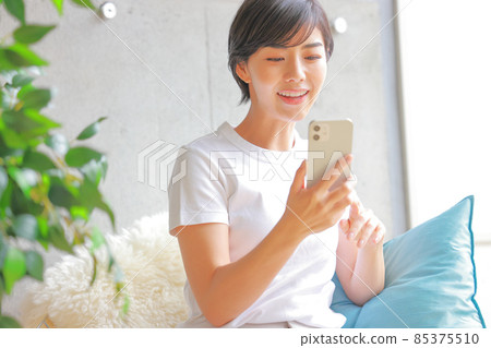 Female looking at a smartphone leaning against a light blue cushion 1 85375510