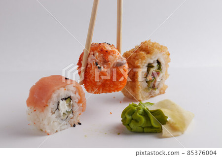 a hand and Chinese chopsticks holds a roll over other sushi, a portion of Asian food, rolls a hand and Chinese chopsticks holds a roll over other sushi, a portion of Asian food, rolls 85376004