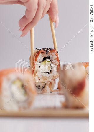 a hand and Chinese chopsticks holds a roll over other sushi, a portion of Asian food, rolls 85376081