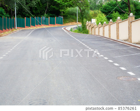 Freshly laid asphalt on the road with markings and fences along and green trees Freshly laid asphalt on the road with markings and fences along and green trees 85376261