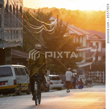 Main street of Chake Chake town, capital of Pemba Island. Man on a bicycle Moving by the road at sunset time Main street of Chake Chake town, capital of Pemba Island. Man on a bicycle Moving by the road at sunset time 85377874