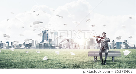 Handsome violinist in park on wooden bench play his melody Handsome violinist in park on wooden bench play his melody 85378402
