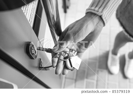 A woman's hand opens the door with a key on which the keychain hangs at home. 85379319