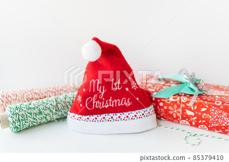 New Year's hat for a baby with the inscription my first Christmas on a background of gifts. New Year's hat for a baby with the inscription my first Christmas on a background of gifts. 85379410