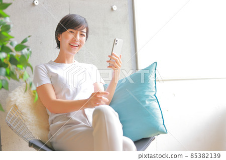 A woman leaning on a light blue cushion and raising her face from her smartphone 2 85382139