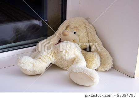A soft toy rabbit lies forgotten on the windowsill 85384793