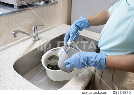 Drainage outlet A male worker in house cleaning who cleans the dust pan with a brush 85384870